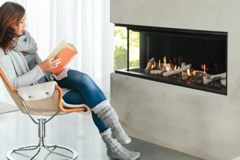 A woman reading a book sits next to a fireplace